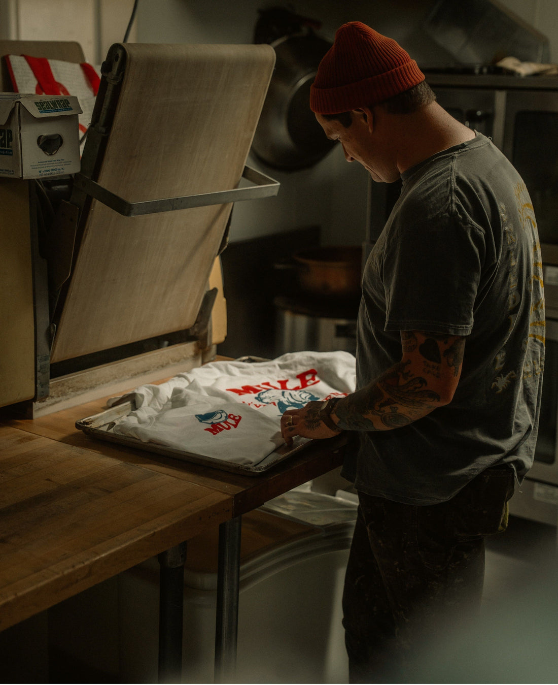 Person bei der Veredelung bedruckter T-Shirts in einer Textilwerkstatt - Beispiel für den Produktionsprozess von Print on Demand.