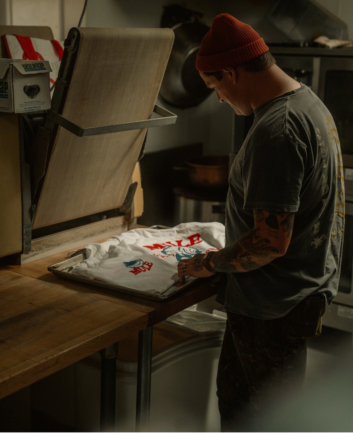 Person bei der Veredelung bedruckter T-Shirts in einer Textilwerkstatt - Beispiel für den Produktionsprozess von Print on Demand.